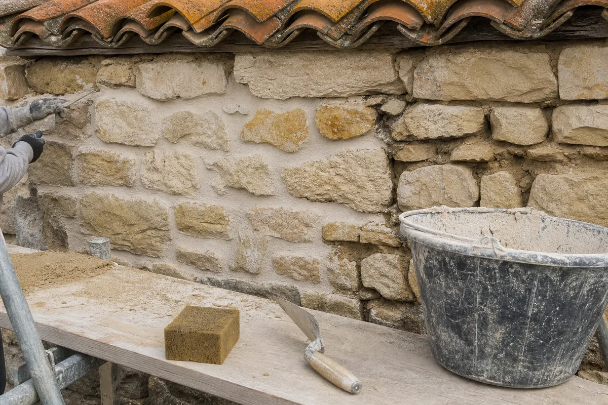 Mur en moellons de pierre calcaire blonde en cours de rejointoiement au mortier de chaux, échafaudage devant la façade