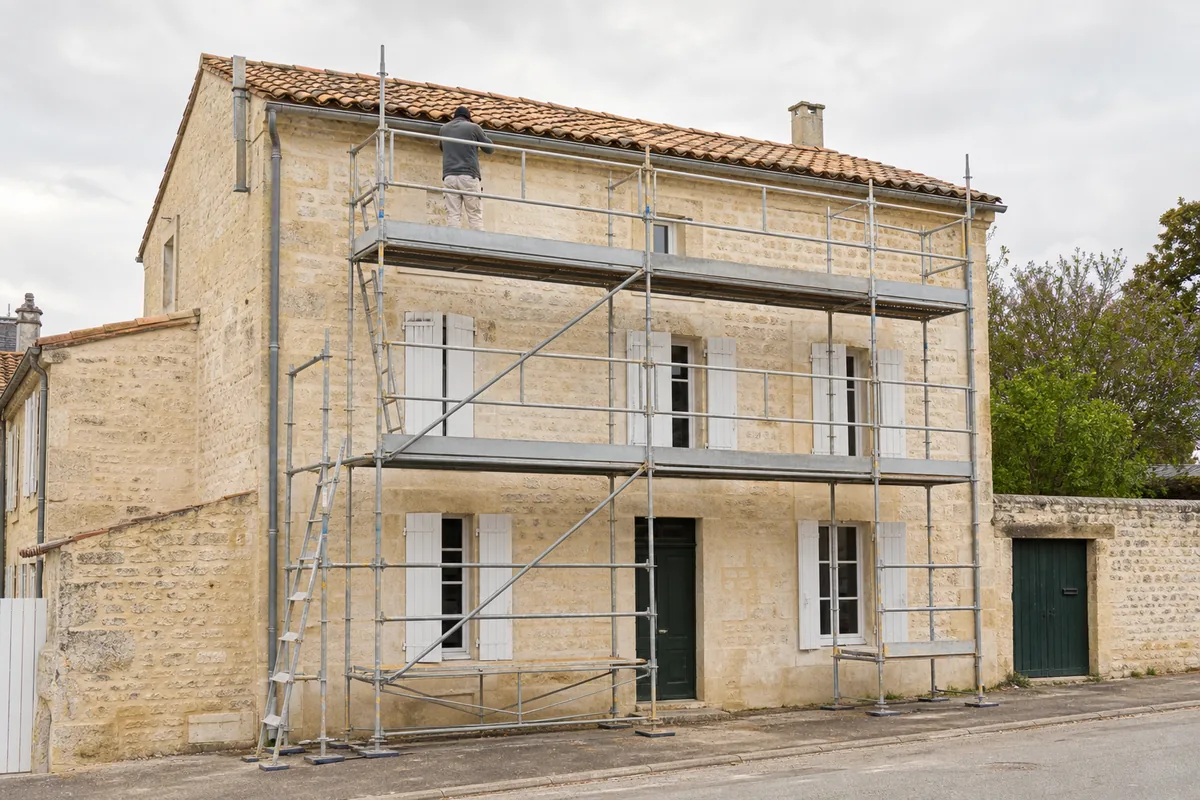 Échafaudage de pied devant une façade en pierre calcaire et une toiture en tuile canal charentaise